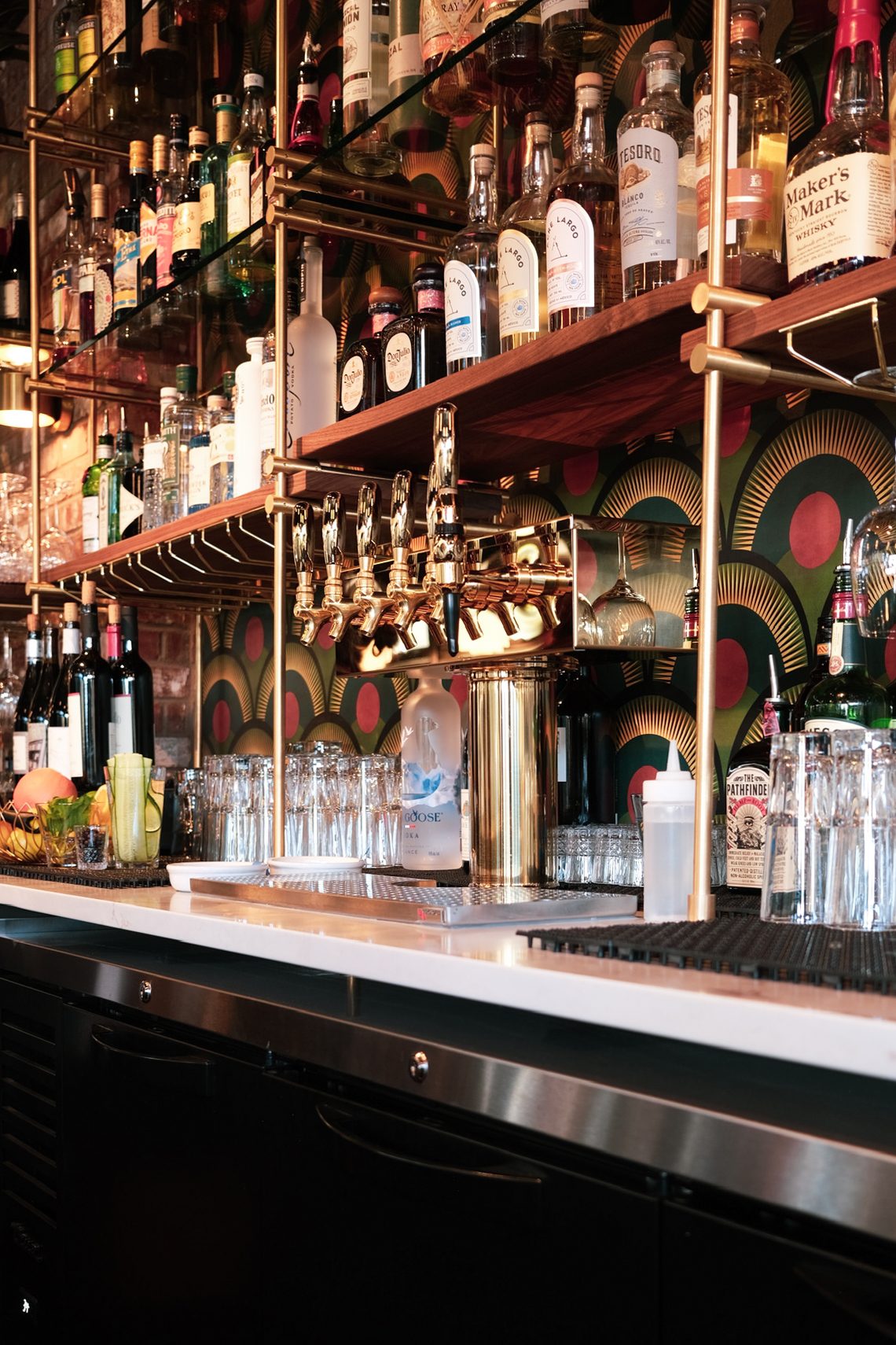 The back bar at Olive & May, stocked and lit against the deco wallpaper